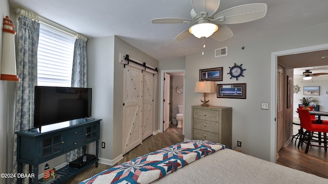 bedroom featuring a barn door, dark hardwood / wood-style floors, ensuite bath, and ceiling fan