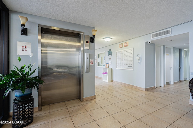 interior space with light tile patterned floors, a textured ceiling, and elevator