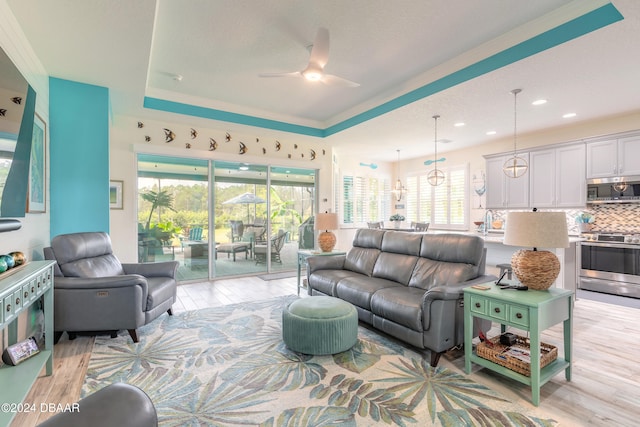 living room featuring light wood-type flooring, ceiling fan, and a raised ceiling