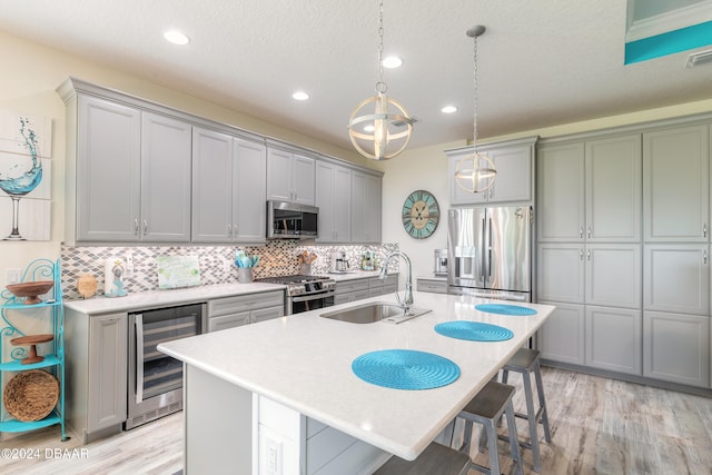 kitchen featuring a center island with sink, beverage cooler, light hardwood / wood-style flooring, sink, and appliances with stainless steel finishes