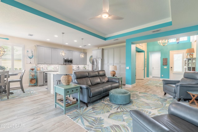 living room featuring ceiling fan with notable chandelier, a raised ceiling, light hardwood / wood-style flooring, and crown molding