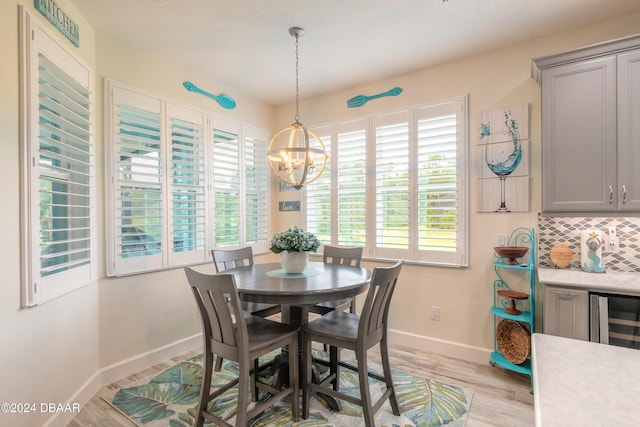 dining room with light wood-type flooring, a notable chandelier, and beverage cooler