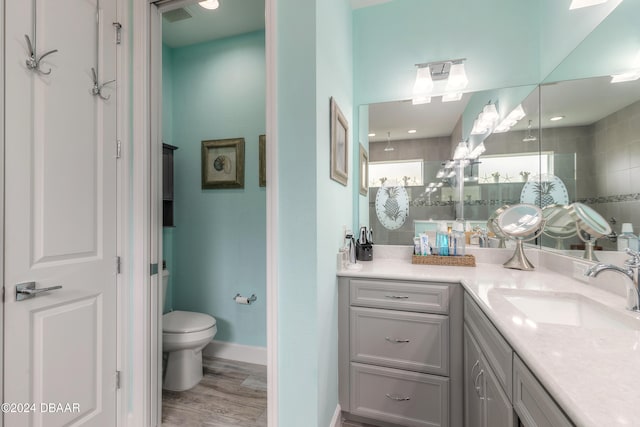 bathroom featuring toilet, vanity, wood-type flooring, and a tile shower