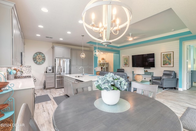 dining space with a notable chandelier, sink, crown molding, a raised ceiling, and light hardwood / wood-style flooring