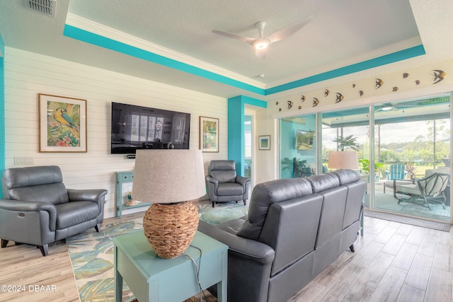 living room featuring a textured ceiling, light hardwood / wood-style flooring, ceiling fan, and a raised ceiling