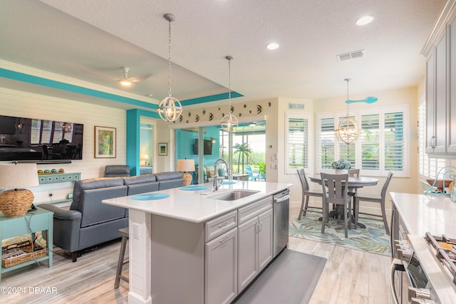 kitchen featuring a healthy amount of sunlight, sink, an island with sink, appliances with stainless steel finishes, and decorative light fixtures