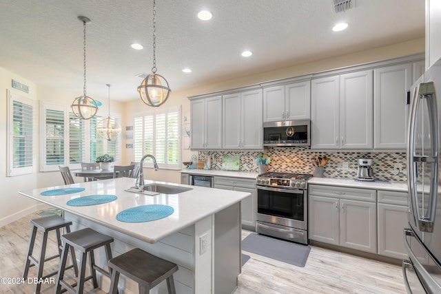 kitchen with a center island with sink, stainless steel appliances, a textured ceiling, decorative light fixtures, and sink