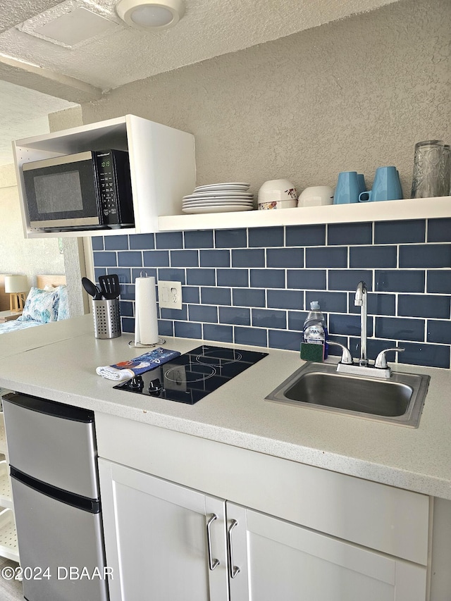 kitchen with black electric stovetop, backsplash, white cabinetry, and sink