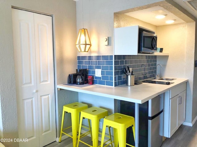 kitchen featuring hardwood / wood-style floors, backsplash, sink, hanging light fixtures, and white cabinetry