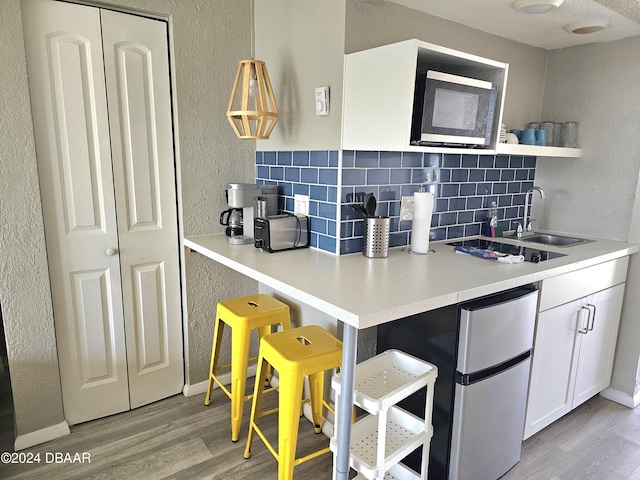 kitchen featuring sink, light hardwood / wood-style flooring, stainless steel fridge, tasteful backsplash, and white cabinetry