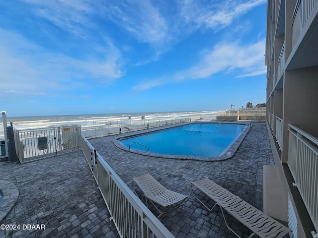 view of swimming pool with a view of the beach, a water view, and a patio area