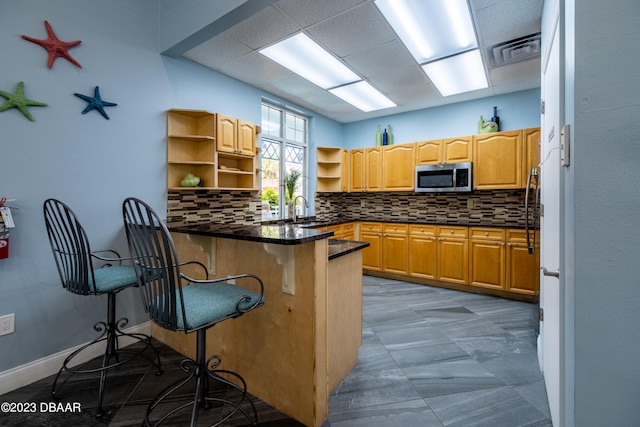 kitchen with kitchen peninsula, a kitchen breakfast bar, tasteful backsplash, and sink