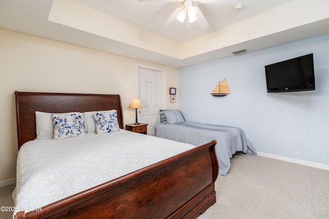 carpeted bedroom with ceiling fan and a raised ceiling