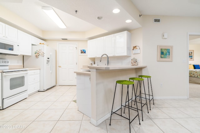 kitchen with white appliances, a breakfast bar area, white cabinetry, and kitchen peninsula