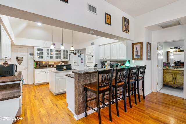 kitchen with white appliances, visible vents, a peninsula, white cabinets, and glass insert cabinets