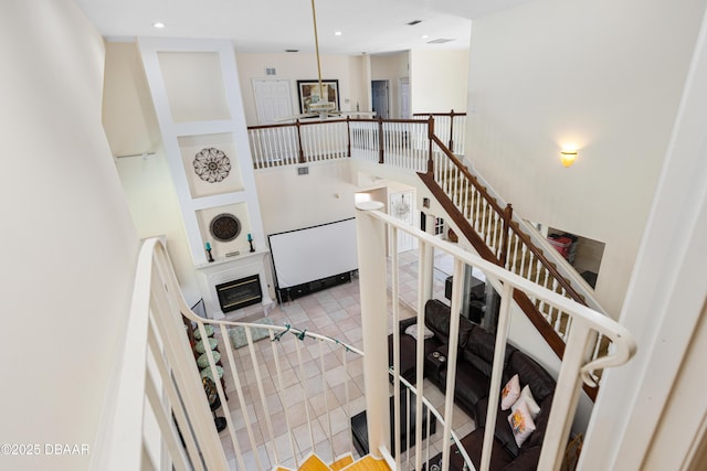 stairs with tile patterned flooring, a glass covered fireplace, recessed lighting, and a high ceiling