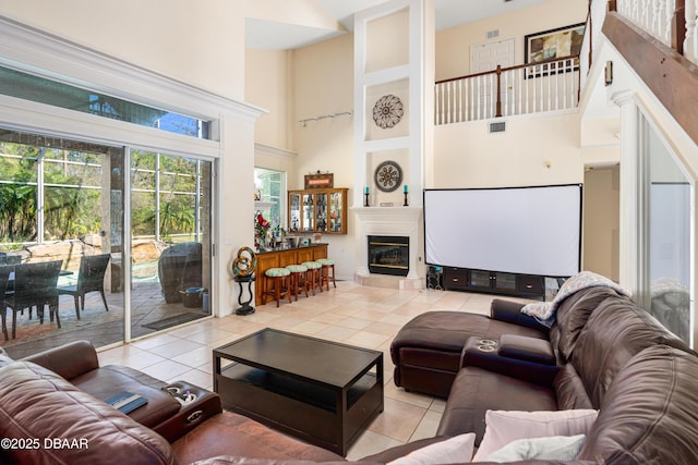 living area featuring light tile patterned floors, visible vents, a tile fireplace, and a towering ceiling