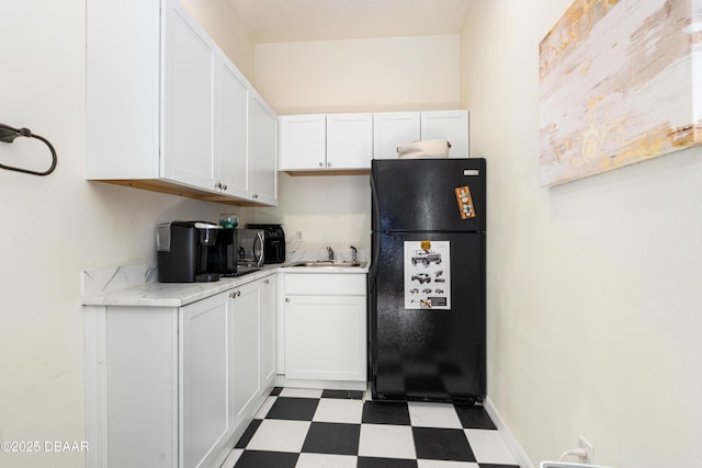 kitchen featuring tile patterned floors, white cabinets, freestanding refrigerator, and a sink