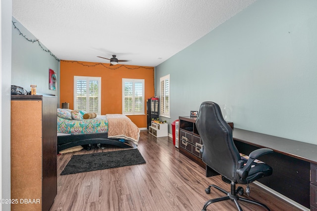 bedroom with ceiling fan, wood finished floors, baseboards, and a textured ceiling