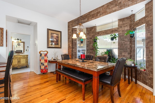 dining area with visible vents, brick wall, baseboards, an inviting chandelier, and light wood-type flooring