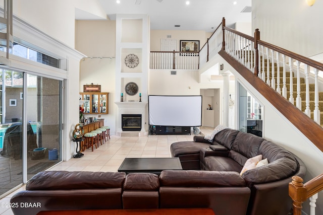 tiled living area with a glass covered fireplace, stairway, and a towering ceiling