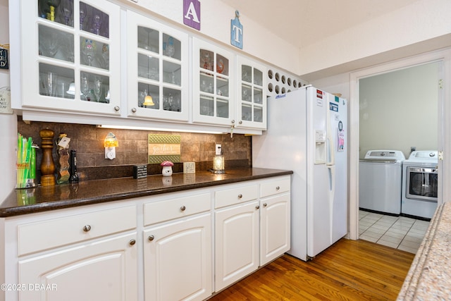 kitchen with independent washer and dryer, tasteful backsplash, white refrigerator with ice dispenser, wood finished floors, and glass insert cabinets