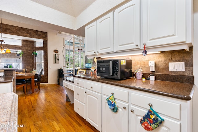 kitchen with tasteful backsplash, light wood-style flooring, white cabinets, and black microwave