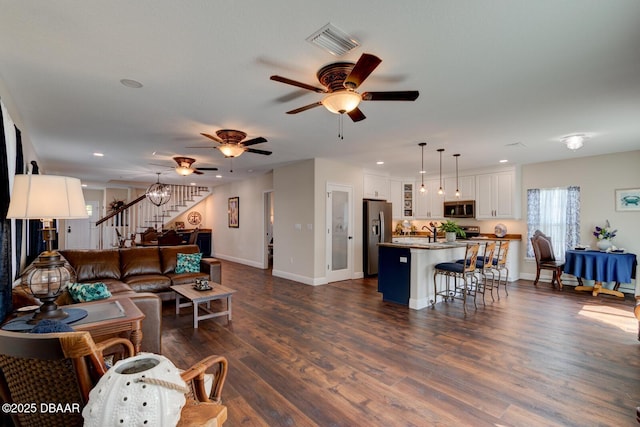 living room with visible vents, a ceiling fan, stairs, baseboards, and dark wood-style flooring