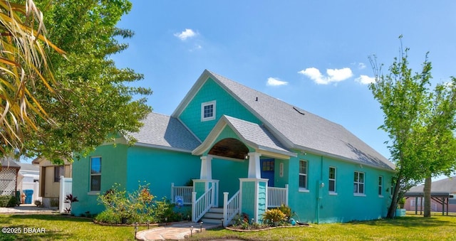 view of front of house featuring stucco siding, a porch, a front yard, and roof with shingles