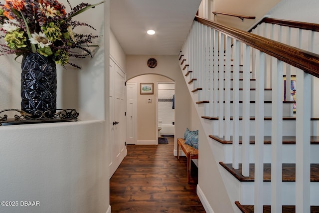 corridor with baseboards, arched walkways, dark wood finished floors, and stairs