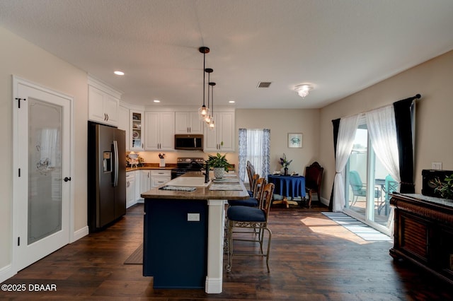 kitchen with visible vents, dark wood finished floors, white cabinets, appliances with stainless steel finishes, and a kitchen bar