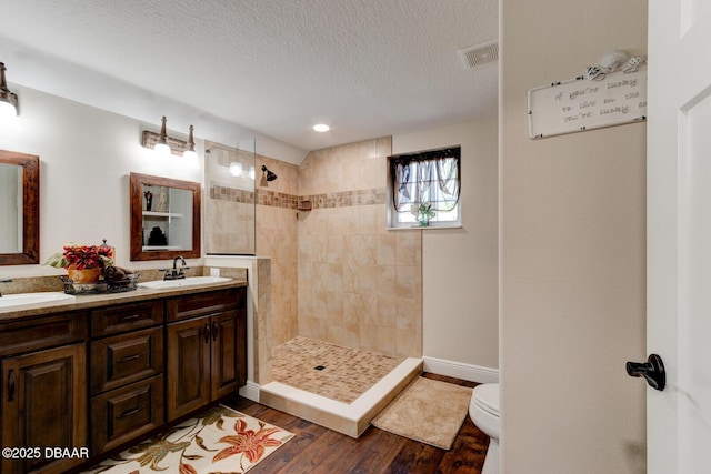 bathroom with wood finished floors, visible vents, a sink, walk in shower, and toilet