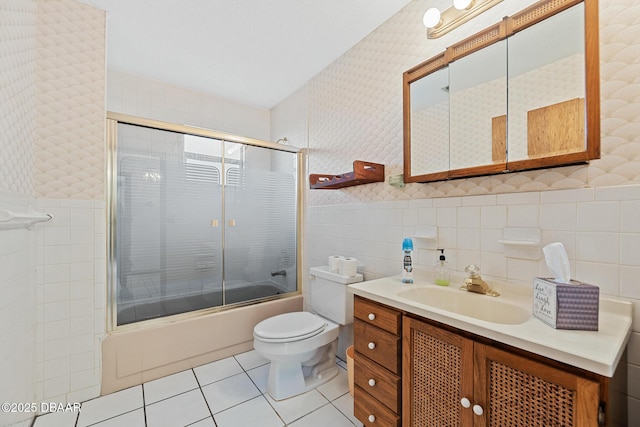 full bathroom featuring toilet, bath / shower combo with glass door, tile walls, vanity, and tile patterned flooring