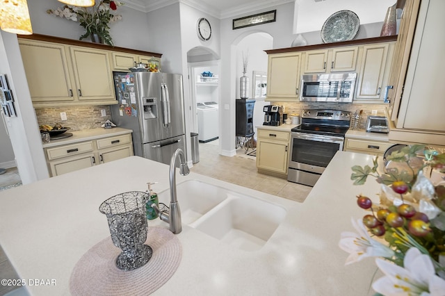 kitchen with decorative backsplash, appliances with stainless steel finishes, ornamental molding, washer and dryer, and cream cabinetry