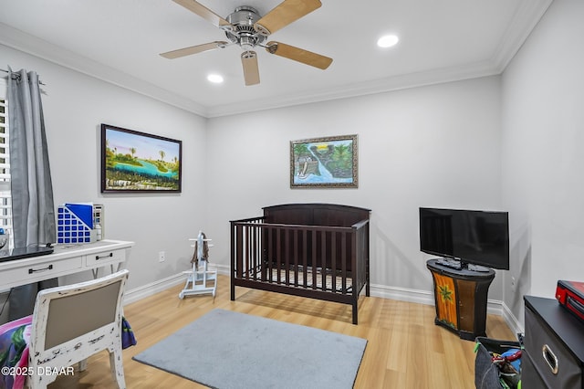 bedroom with ceiling fan, crown molding, light hardwood / wood-style floors, and a crib