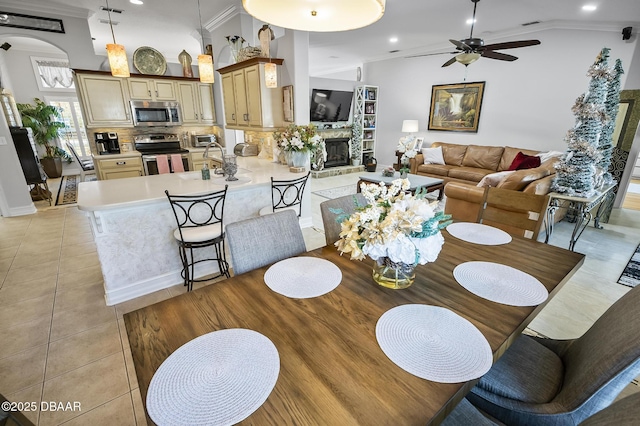 dining room featuring a stone fireplace, crown molding, vaulted ceiling, ceiling fan, and light tile patterned floors