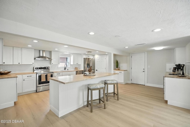 5540 W Bayshore Dr, Port Orange, FL 32127 - kitchen featuring appliances with stainless steel finishes, wall chimney exhaust hood, light wood-style floors, a kitchen breakfast bar, and white cabinets