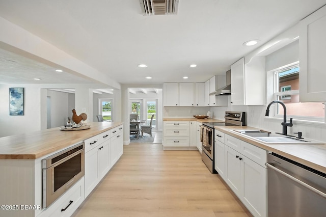 5540 W Bayshore Dr, Port Orange, FL 32127 - kitchen featuring appliances with stainless steel finishes, butcher block counters, wall chimney range hood, light wood-style floors, and recessed lighting