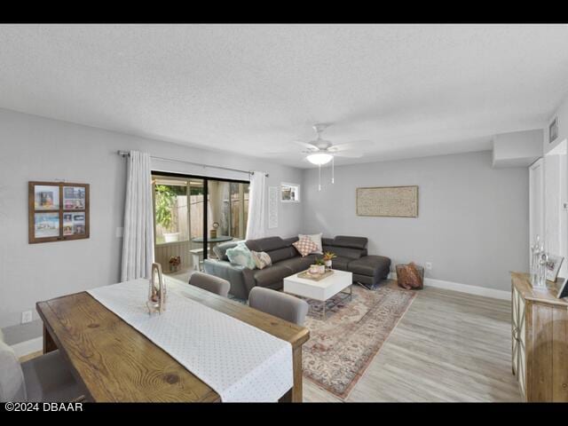 living room featuring ceiling fan, light hardwood / wood-style flooring, and a textured ceiling