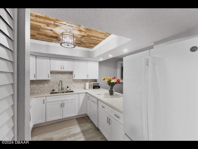 kitchen with sink, backsplash, white cabinets, a tray ceiling, and white appliances