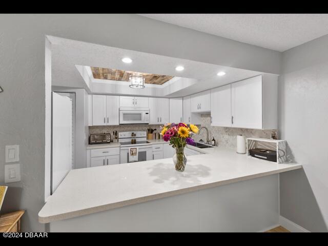 kitchen with kitchen peninsula, white cabinetry, sink, a tray ceiling, and white appliances