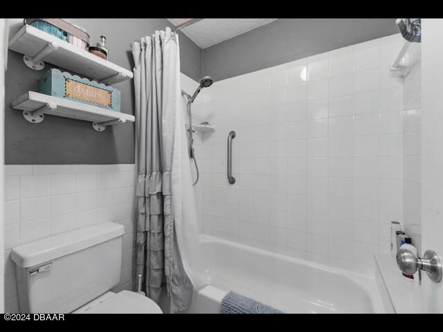 bathroom with shower / bathtub combination with curtain, toilet, tile walls, and a textured ceiling