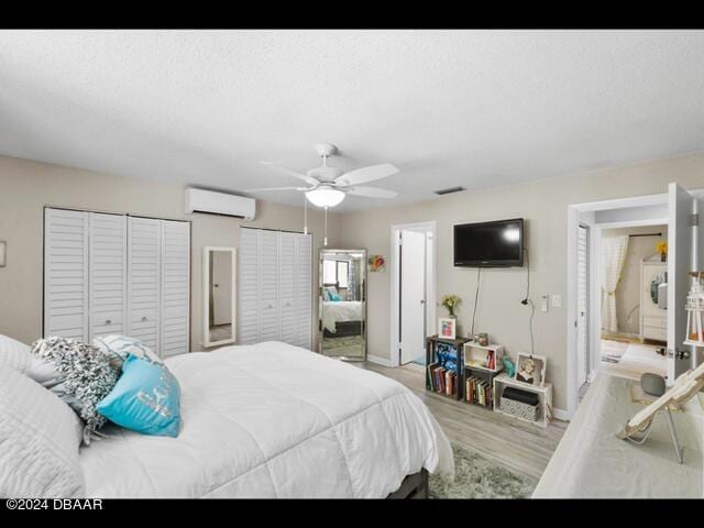 bedroom featuring ceiling fan, a textured ceiling, a wall unit AC, and light hardwood / wood-style flooring