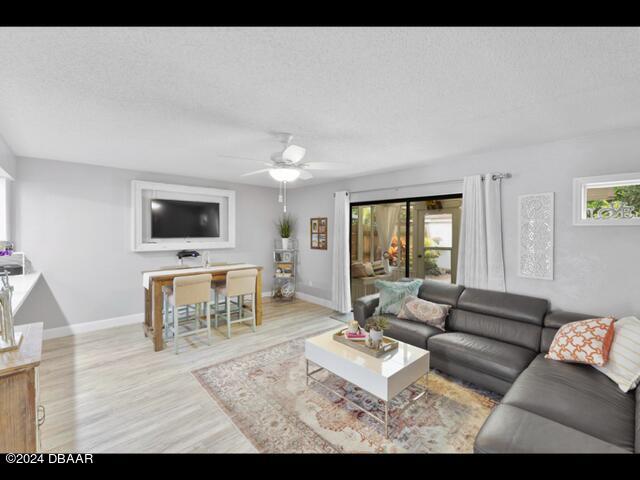 living room with ceiling fan, a textured ceiling, and light hardwood / wood-style flooring