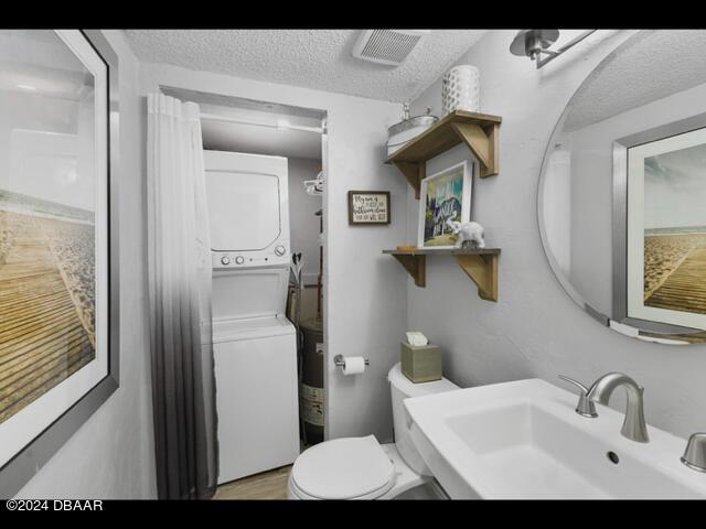 bathroom featuring stacked washer / drying machine, toilet, sink, and a textured ceiling