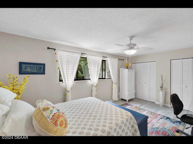 bedroom featuring ceiling fan, two closets, a textured ceiling, and light hardwood / wood-style floors