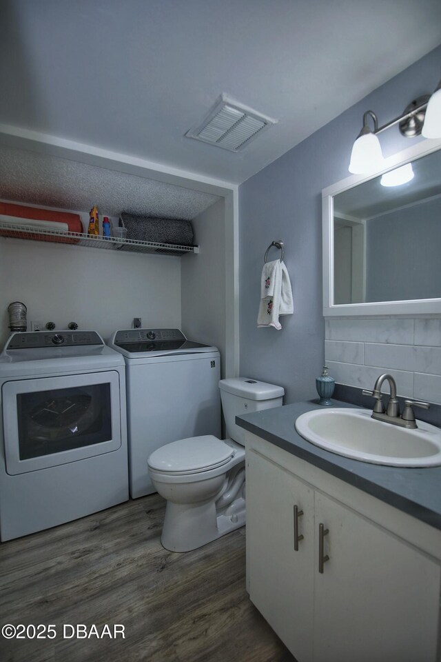 219 Club House Blvd Unit 219, New Smyrna Beach, FL 32168 - bathroom featuring washer and clothes dryer, tasteful backsplash, toilet, vanity, and wood finished floors
