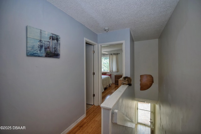 219 Club House Blvd Unit 219, New Smyrna Beach, FL 32168 - hall with light wood-type flooring, a textured ceiling, baseboards, and an upstairs landing