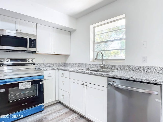 kitchen with light stone counters, white cabinetry, appliances with stainless steel finishes, light wood-type flooring, and sink