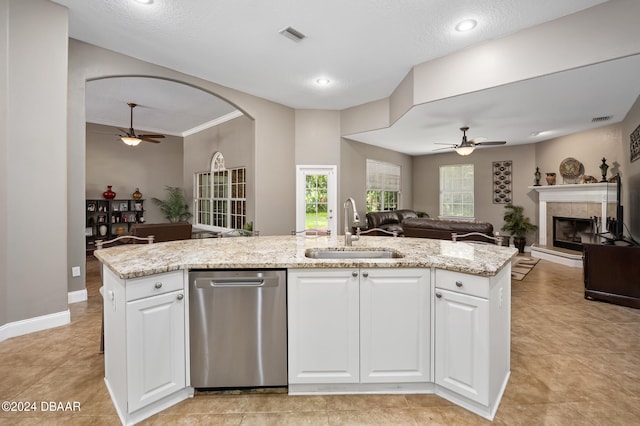 kitchen featuring a tiled fireplace, white cabinetry, sink, a kitchen island with sink, and dishwasher